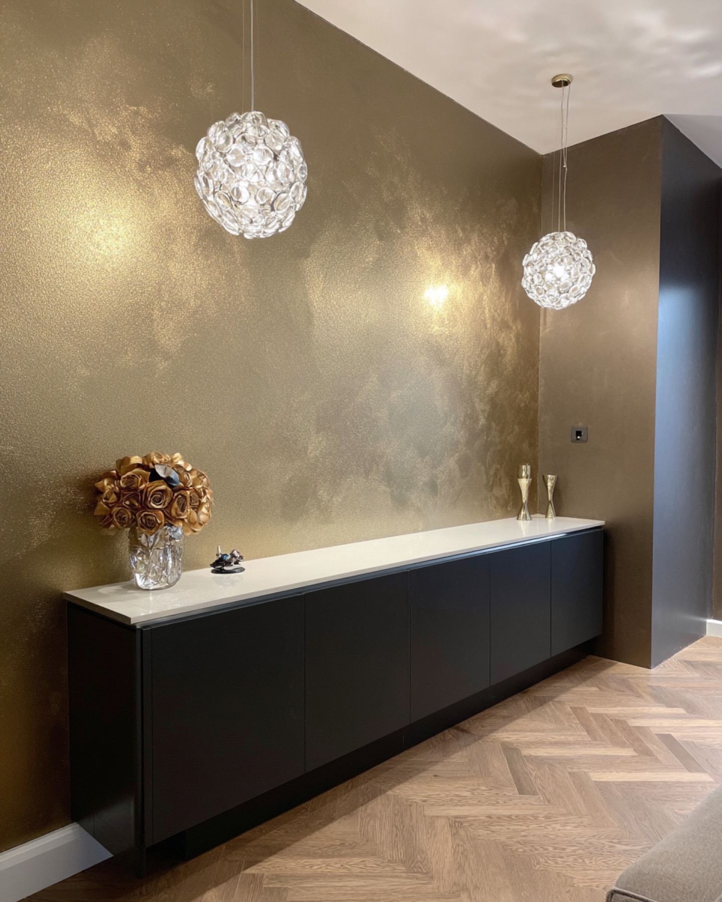 Donkere pearlescent wand met warme gouden gloed onder kristallen hanglampen in entree Blaricum